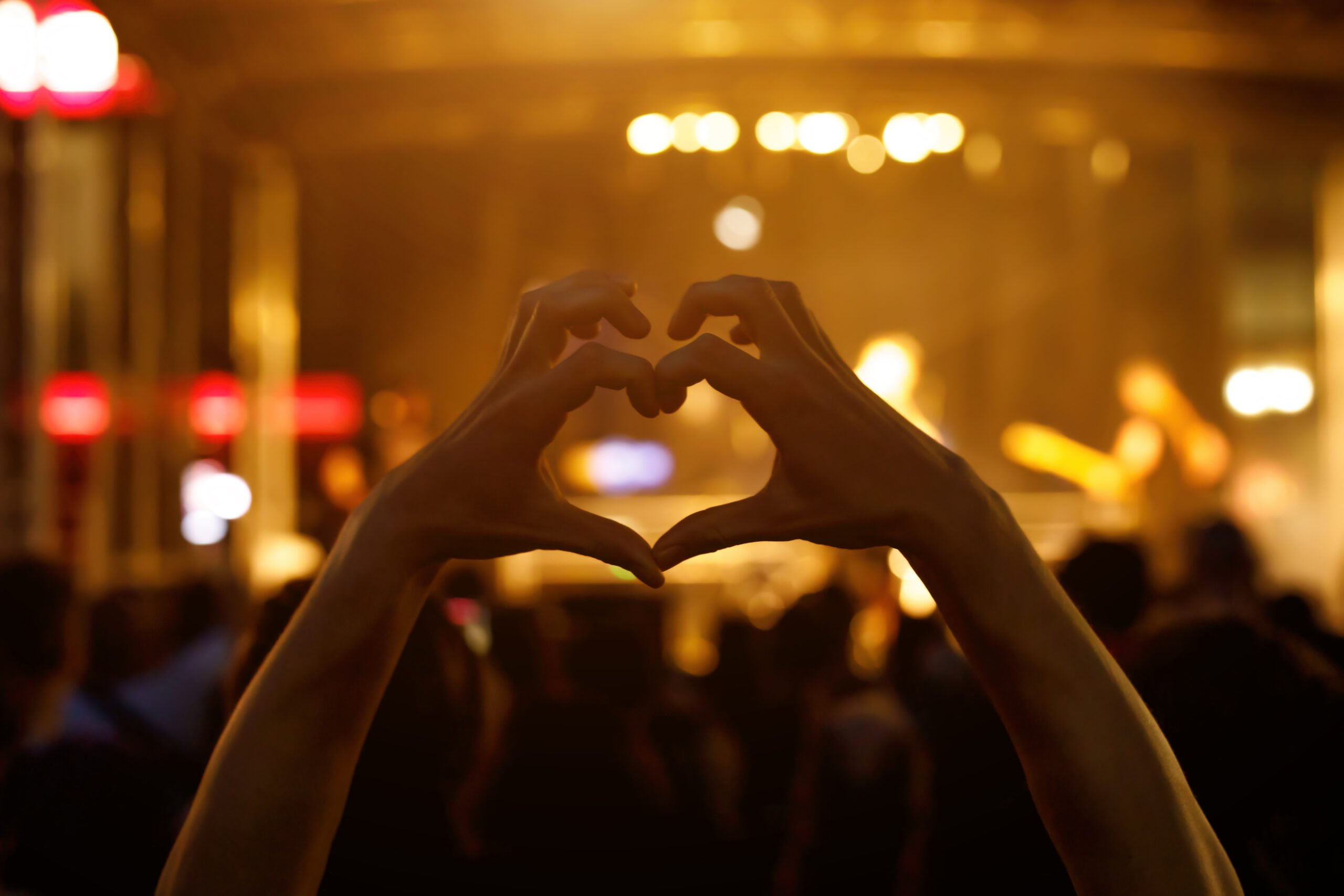 A person is making a heart sign during a concert of a favorite music band. Black silhouette.